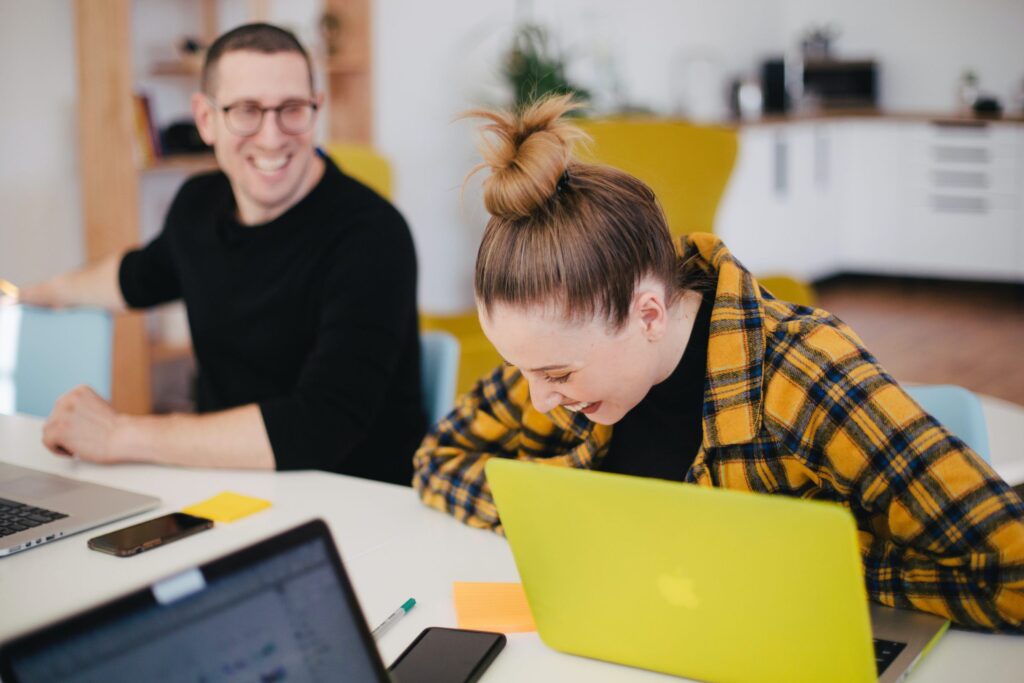 two colleagues laughing over a laptop in the workplace