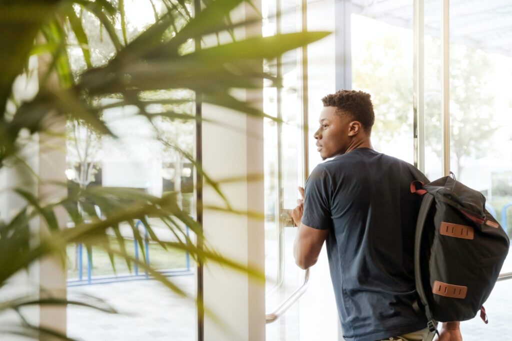 A man with a backpack opens a door to leave a building