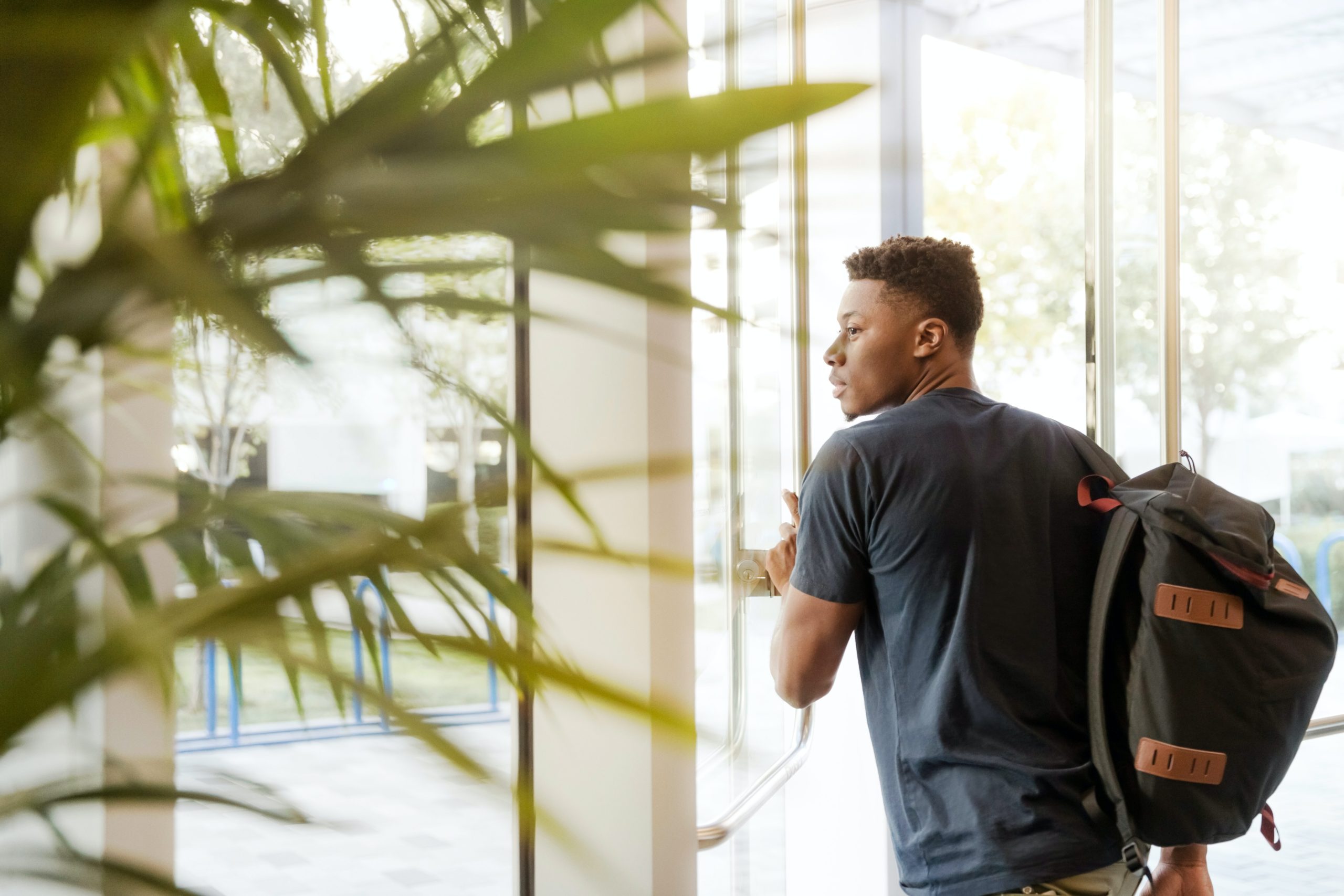 A man with a backpack opens a door to leave a building