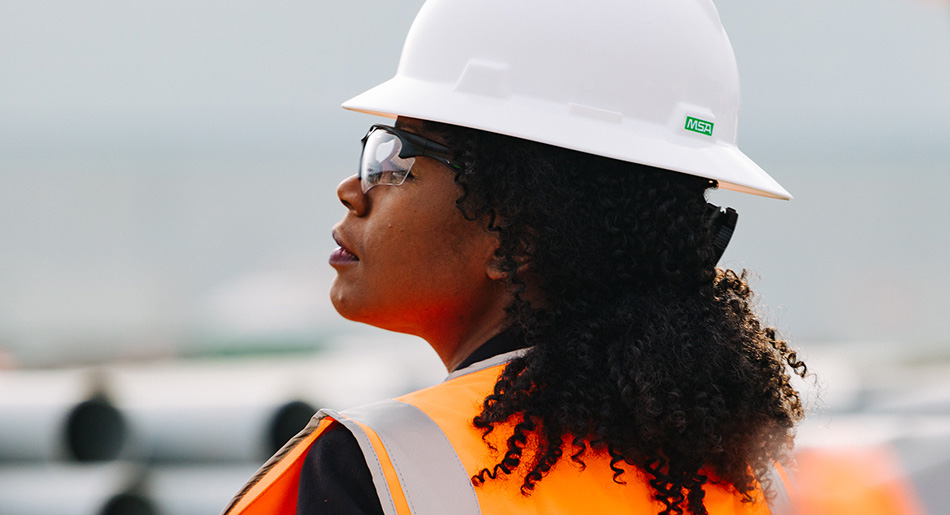 Profile of a Black woman in a hard hat, vest, and safety goggles