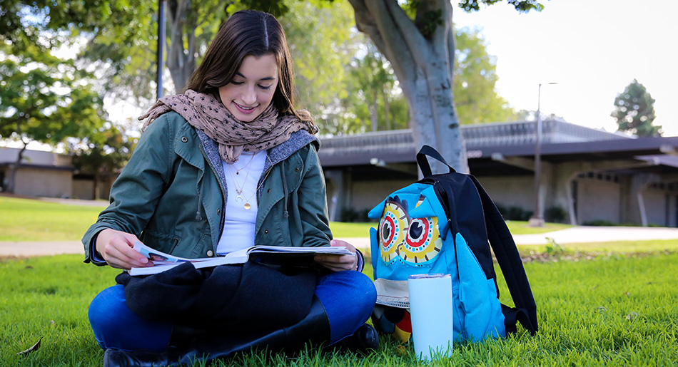 A student sitting on the campus lawn reads a book